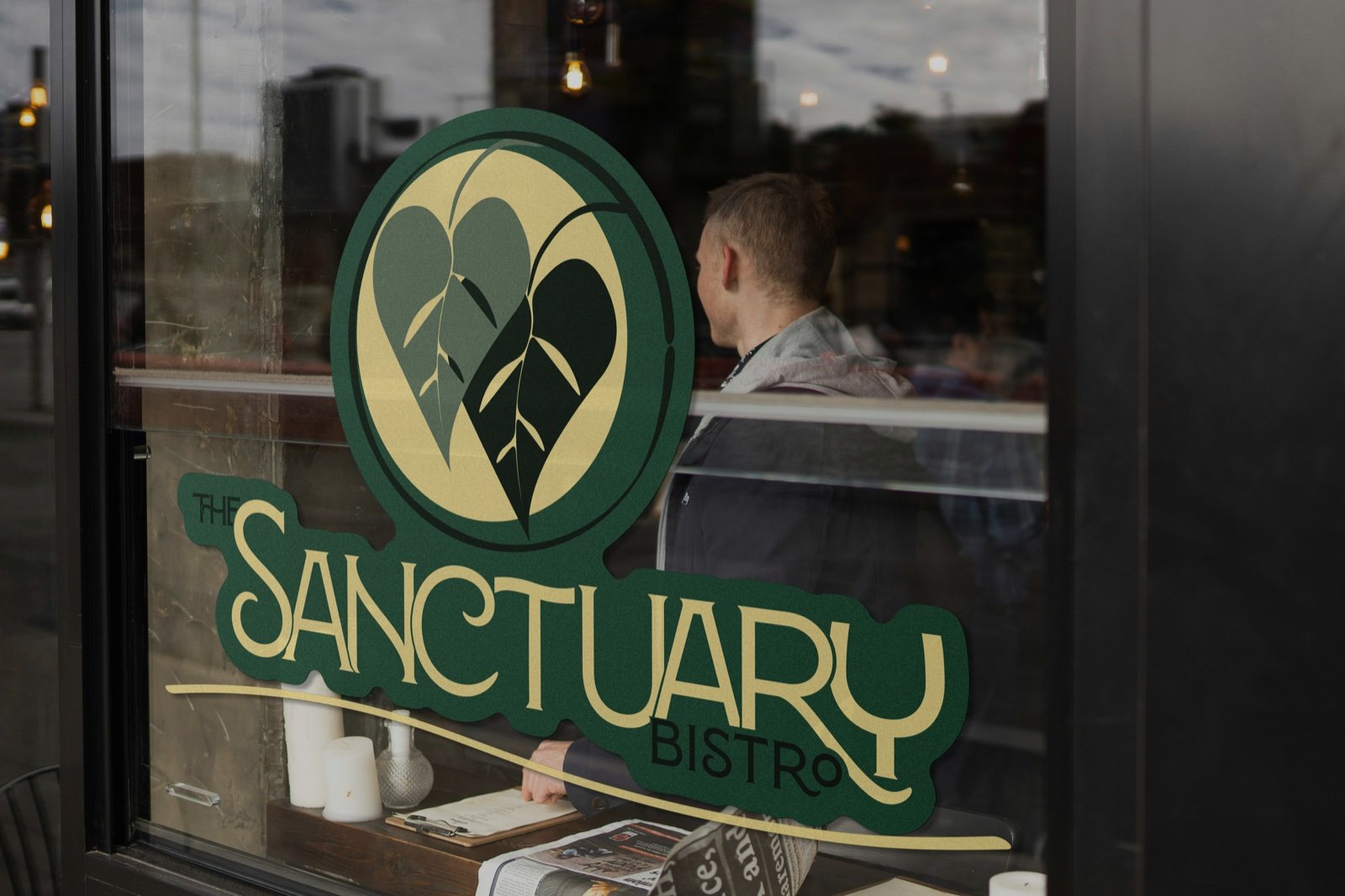Sanctuary Bistro window decal in green and gold on storefront glass with a guest visible inside