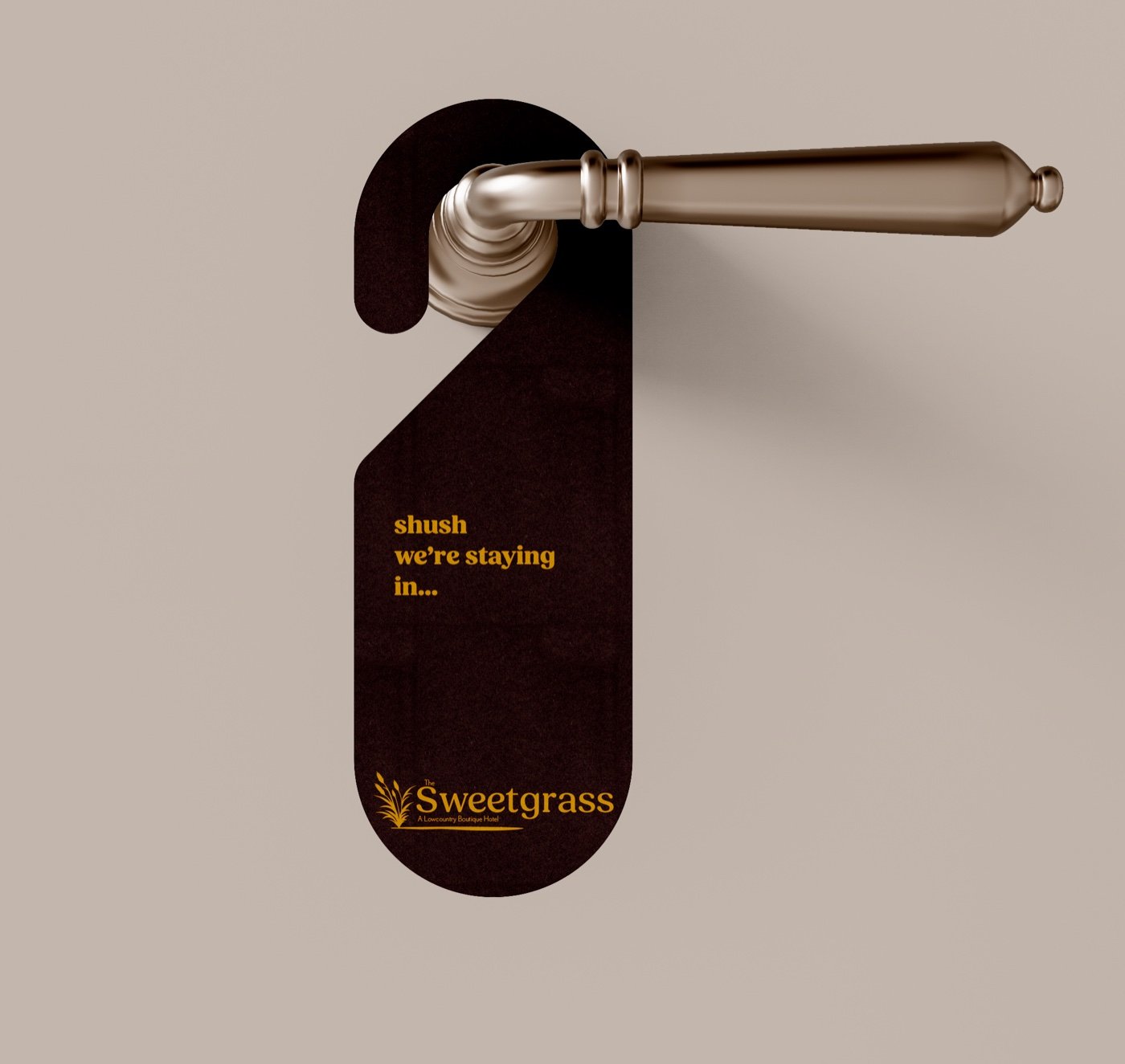 Dark brown do-not-disturb hanger on a brass door handle reading shush, we&rsquo;re staying in, with the gold Sweetgrass logo
