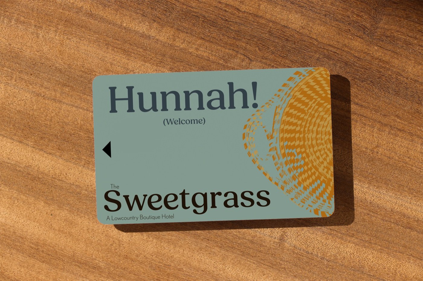 Sea-green Sweetgrass key card reading Hunnah! with Welcome beneath, patterned with a woven basket motif and cut with the same tactile notch