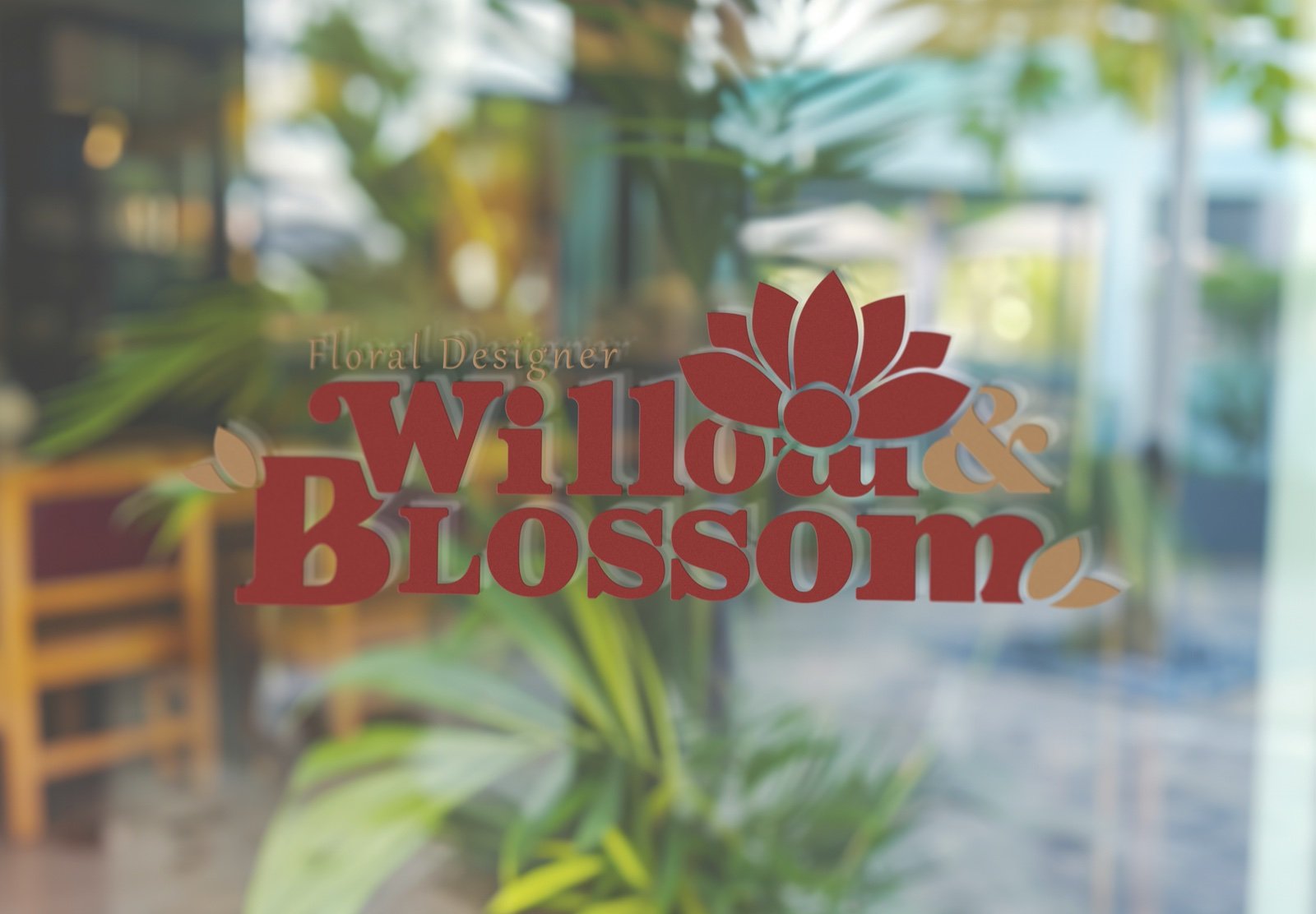 Willow & Blossom window decal in crimson and gold on storefront glass reflecting greenery and cafe chairs